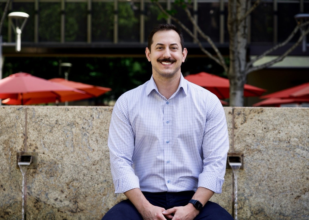 Mike Sertic, seated outdoors in a light checked shirt, smiling